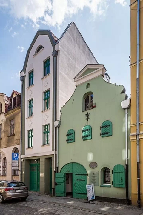 Zielony smukły budynek, czyli Muzeum Podróżników w Toruniu, który mieści się w zabytkowej kamienicy.